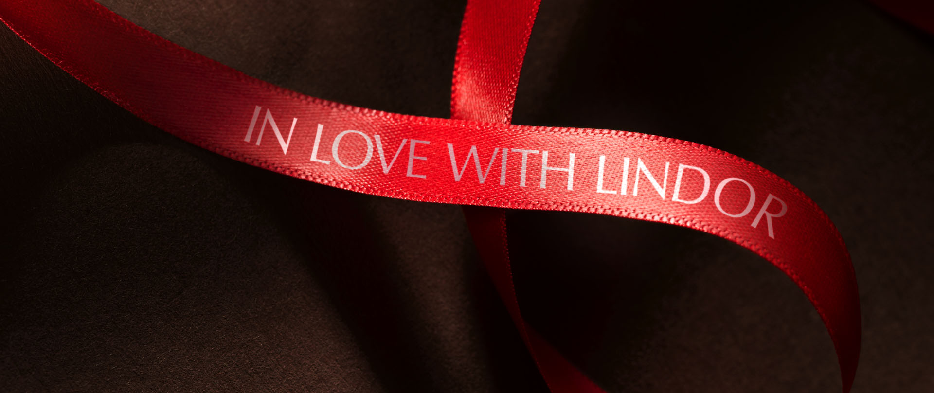 A red bow with the text “In love with LINDOR” on a brown silky background (Photo)